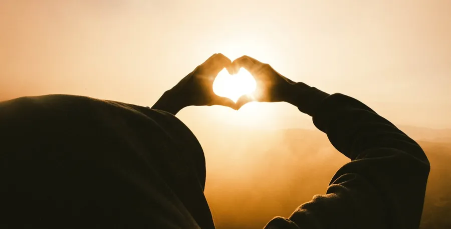 manos formando un corazón y el sol de fondo